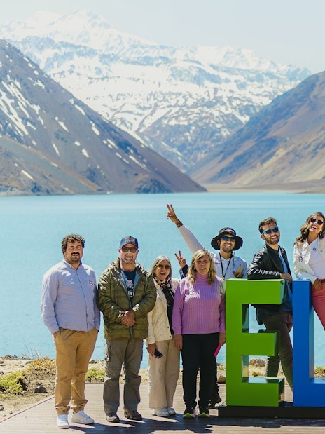 Group enjoying a tour at Embalse El Yeso, Chile, with mountains and lake in the background.