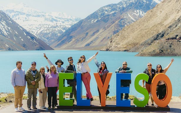 Group enjoying a tour at Embalse El Yeso, Chile, with mountains and lake in the background.
