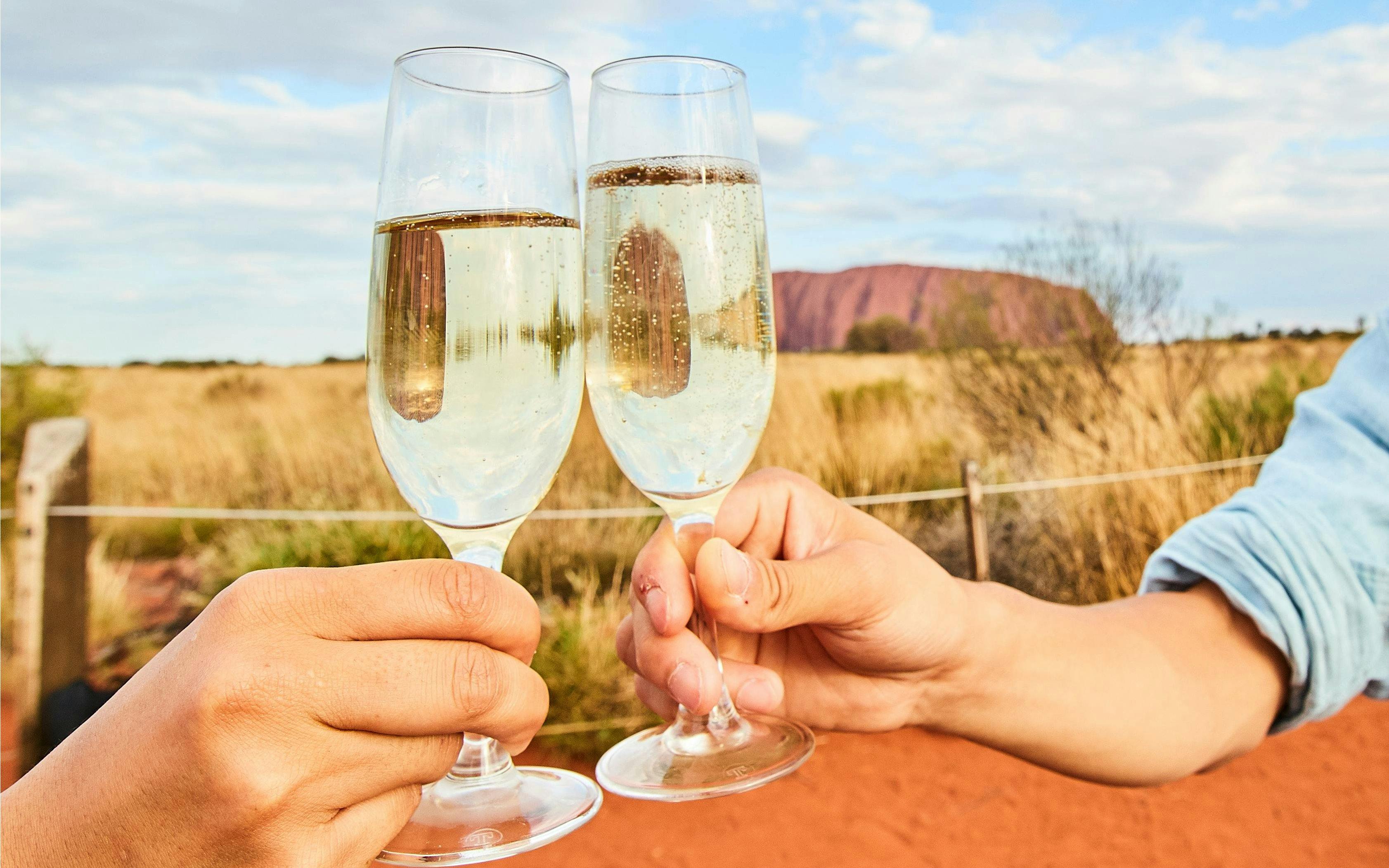 Toasting champagne glasses with Uluru in the background during sunset tour.