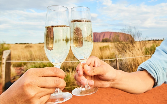 Toasting champagne glasses with Uluru in the background during sunset tour.