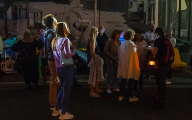 Group of people on a nighttime guided tour in Sydney, listening to a guide holding a lantern.