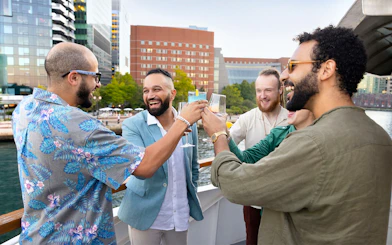 Group toasting on a Boston harbor cruise with city skyline in background.