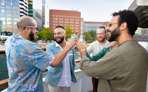 Group toasting on a Boston harbor cruise with city skyline in background.