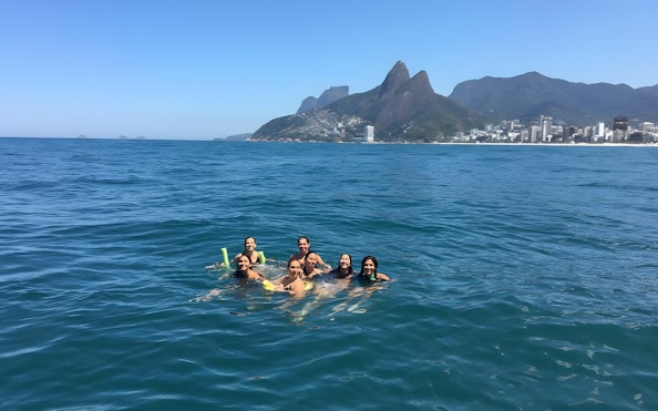 Tourists swimming in the ocean with Rio de Janeiro's mountains in the background.