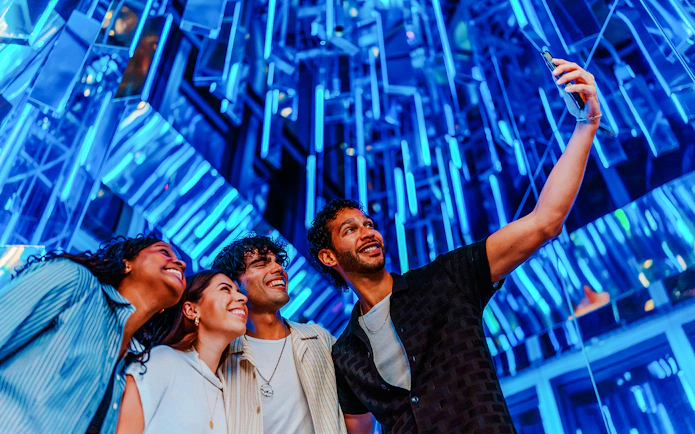 Group taking a selfie at Edge NYC Observation Deck with blue lights in the background.