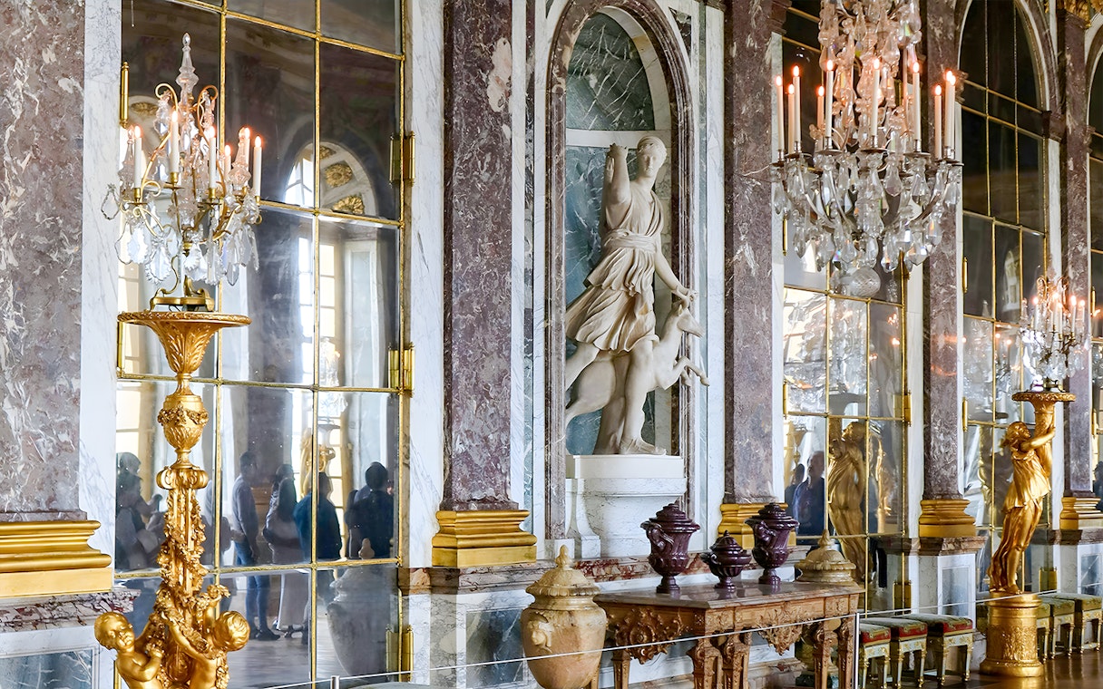 Palace of Versailles interior with ornate chandeliers and marble statues, France.