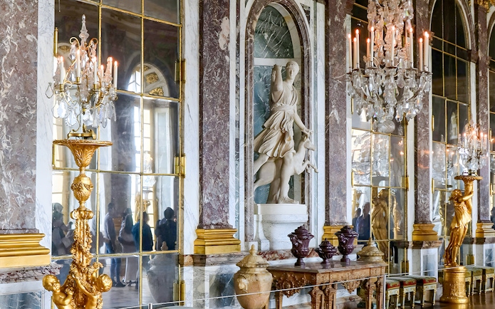 Palace of Versailles interior with ornate chandeliers and marble statues, France.