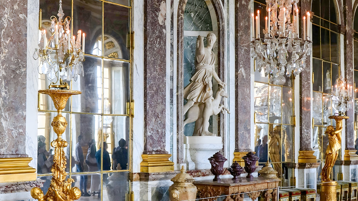Palace of Versailles interior with ornate chandeliers and marble statues, France.