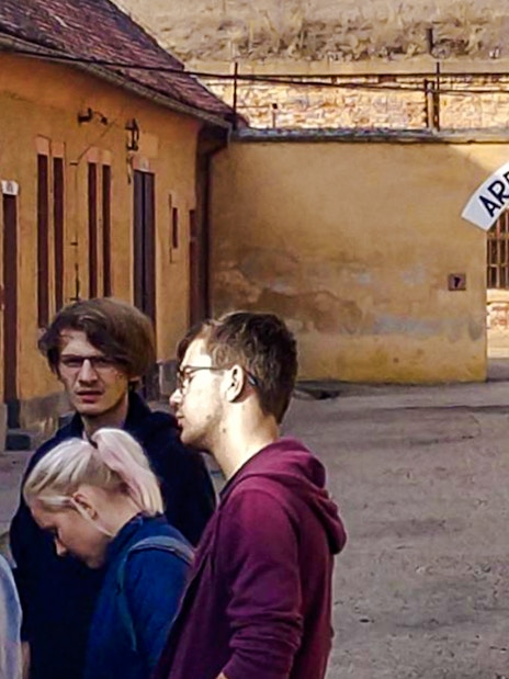Guests exploring Terezin Concentration Camp courtyard under "Arbeit Macht Frei" sign.