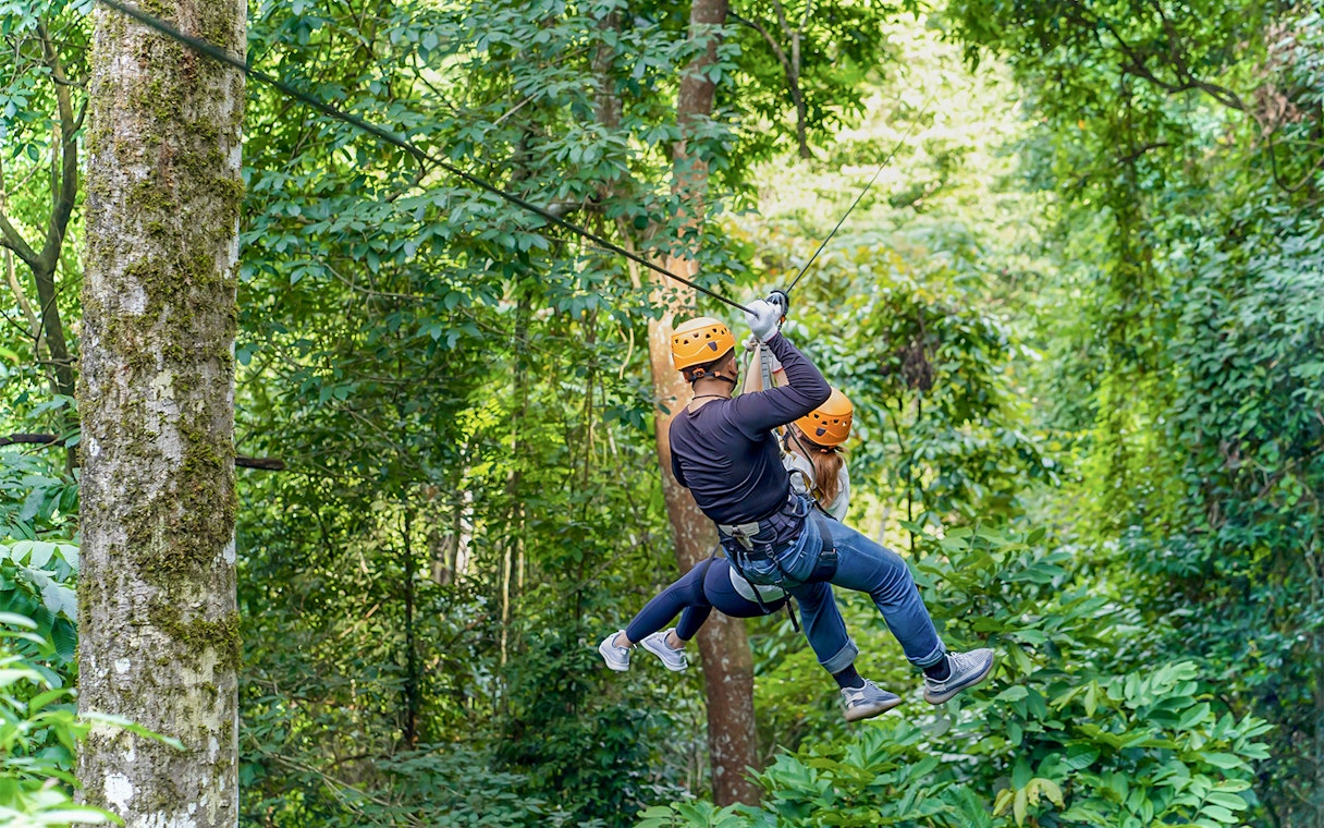 Two people ziplining through lush forest in Phuket.