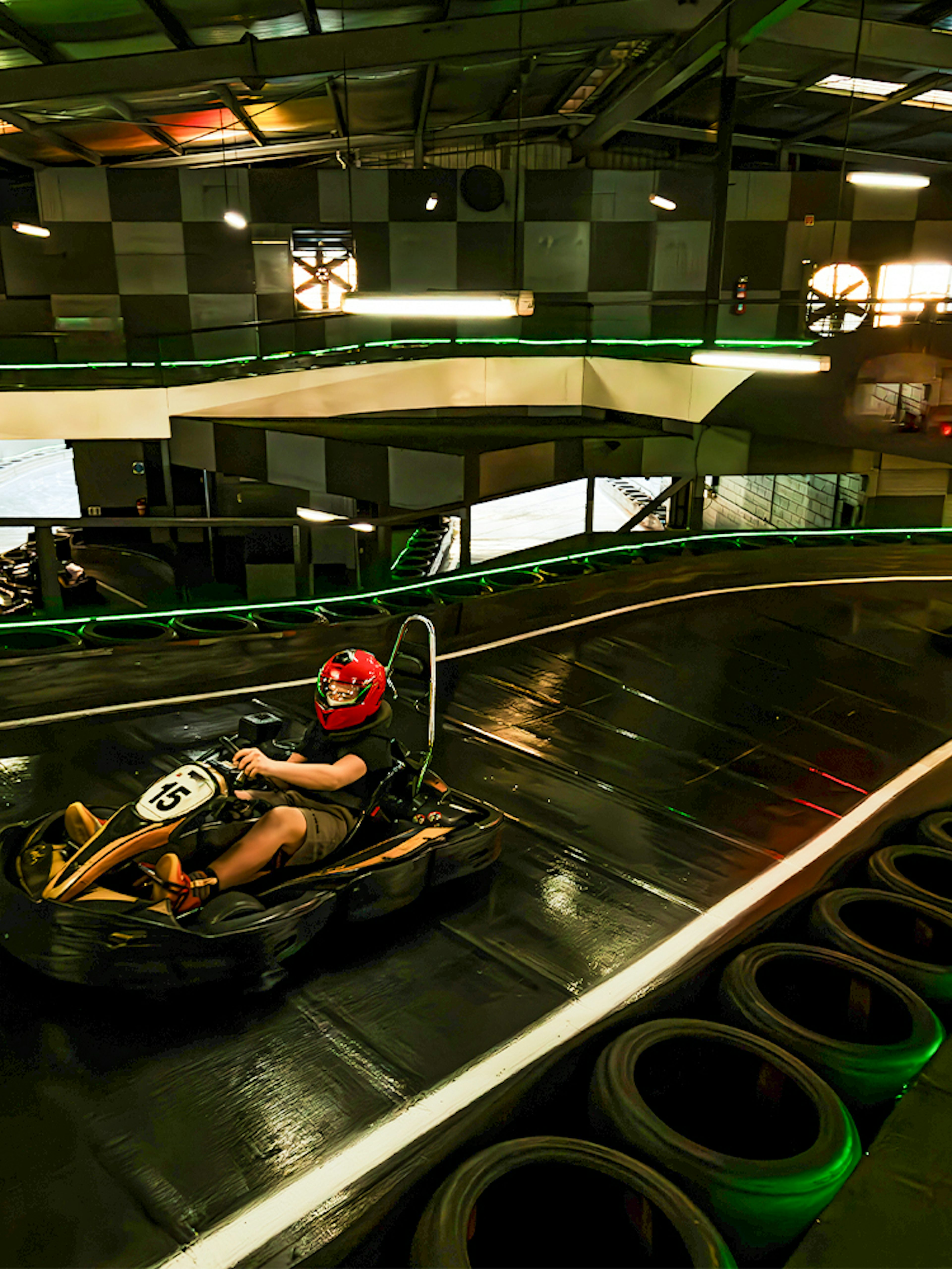 Indoor karting track with racers wearing helmets navigating a curve.