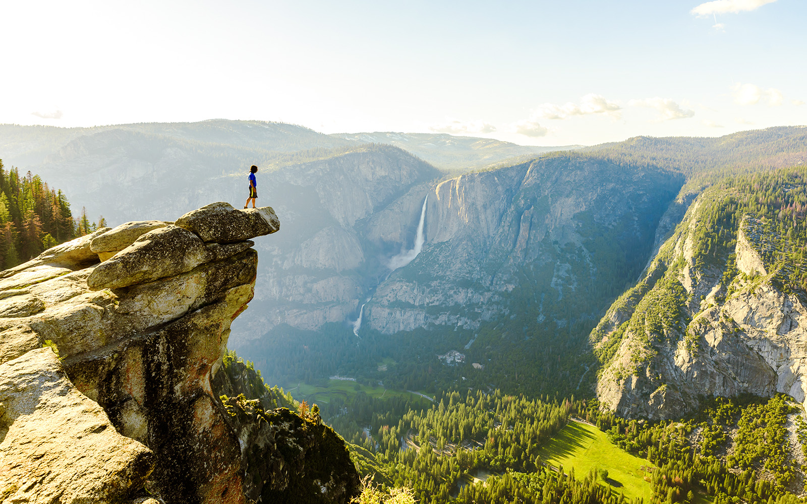 Hiker standing on Glacier Point overlooking Yosemite Falls and Valley in Yosemite National Park.
