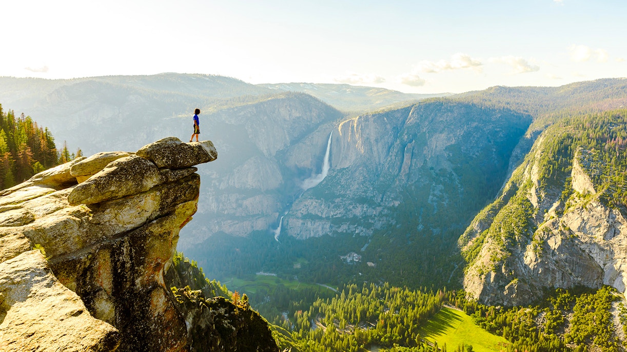 Hiker standing on Glacier Point overlooking Yosemite Falls and Valley in Yosemite National Park.