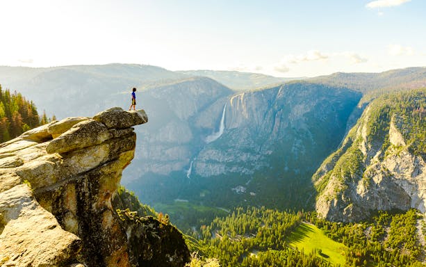 Hiker standing on Glacier Point overlooking Yosemite Falls and Valley in Yosemite National Park.