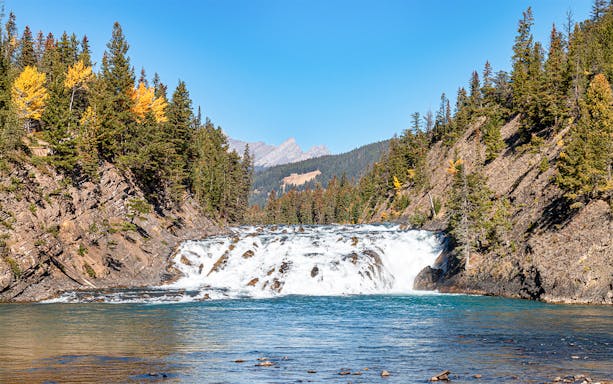 Bow Falls cascading in Banff, Canada, surrounded by forested cliffs and distant mountains.