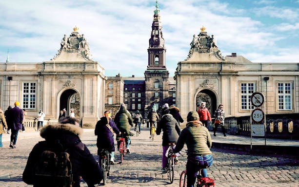 Cyclists approaching Christiansborg Palace entrance on a Copenhagen bike tour.