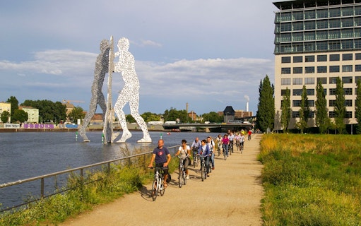 Cyclists on a guided tour near Molecule Man sculpture along the Spree River in Berlin.