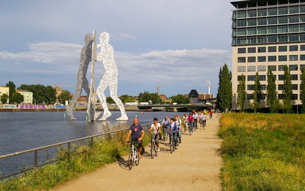Cyclists on a guided tour near Molecule Man sculpture along the Spree River in Berlin.