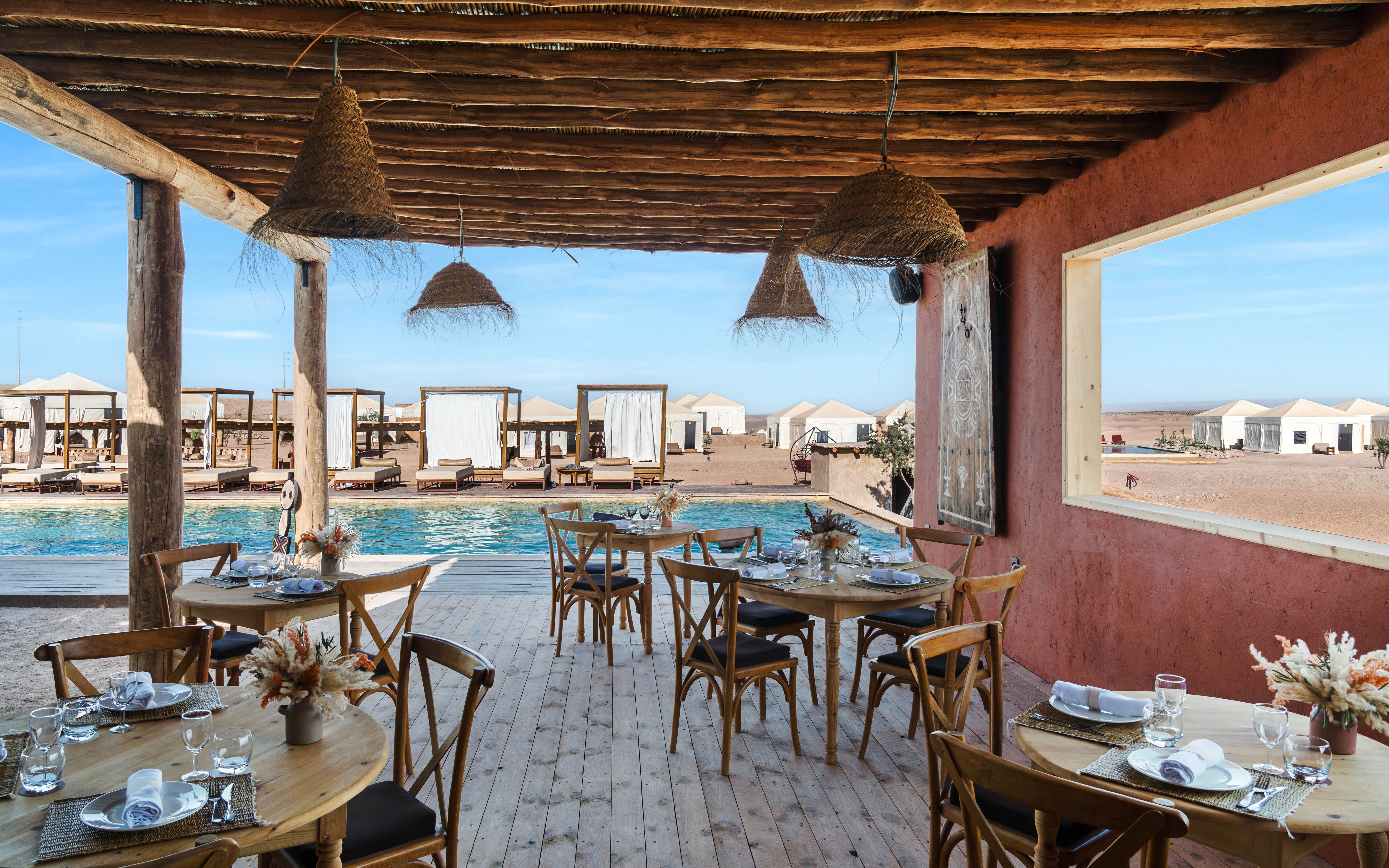 Outdoor dining area overlooking pool and desert tents at Les Terrasses d'Agafay camp.
