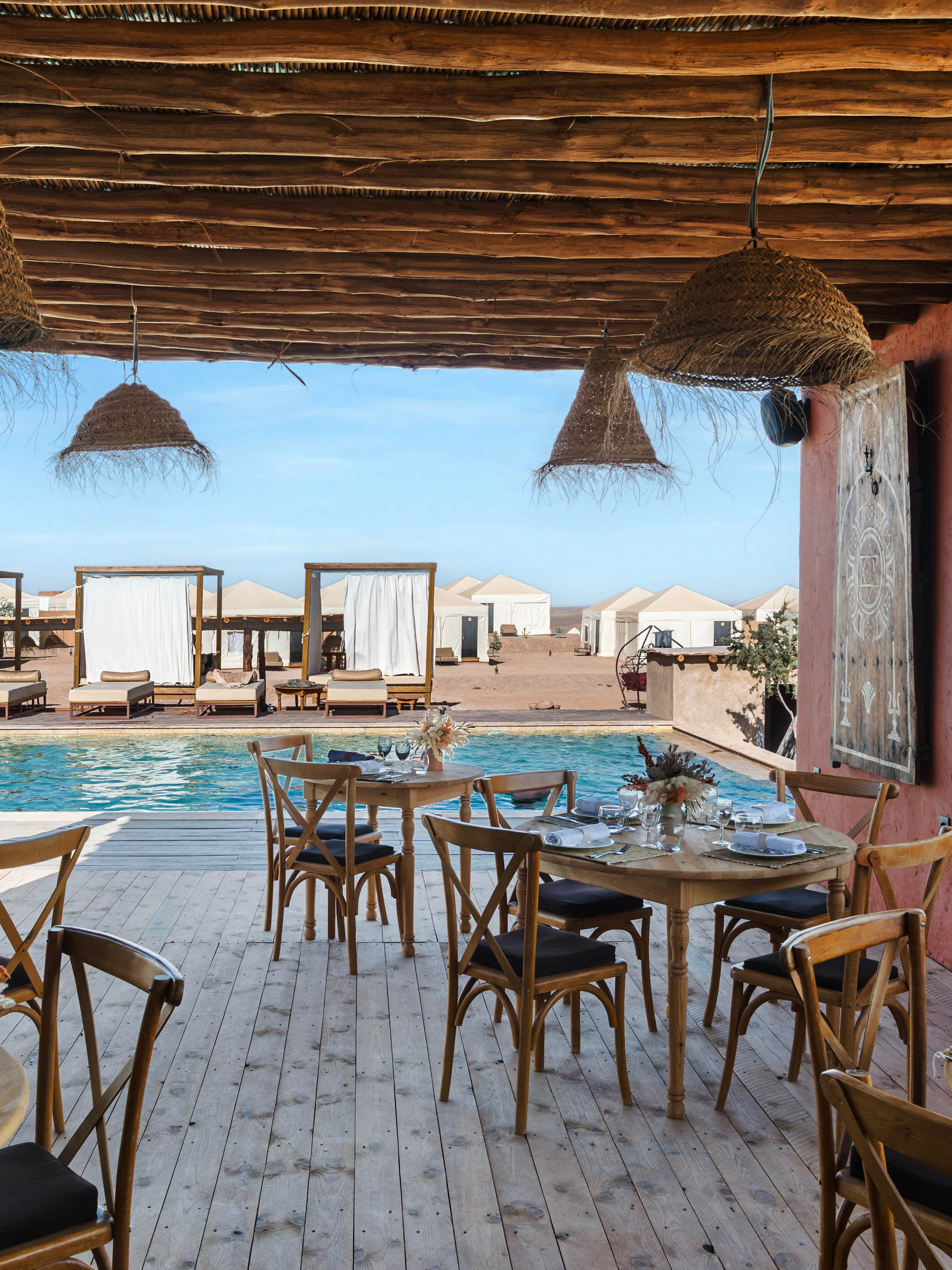 Outdoor dining area overlooking pool and desert tents at Les Terrasses d'Agafay camp.