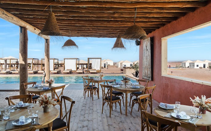Outdoor dining area overlooking pool and desert tents at Les Terrasses d'Agafay camp.
