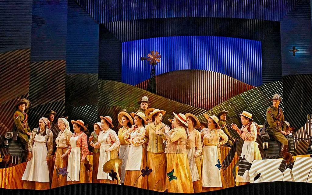 Opera performers on stage in a scene from "The Elixir of Love" with a colorful backdrop.