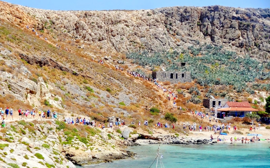 Tourists hiking on Gramvousa Island with stone ruins and rocky landscape.