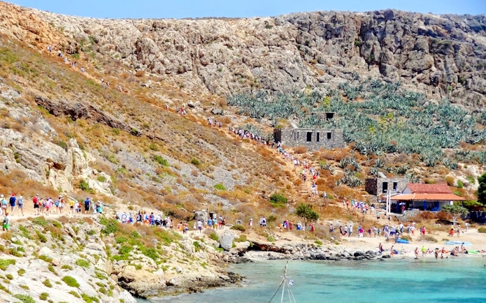 Tourists hiking on Gramvousa Island with stone ruins and rocky landscape.