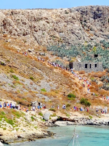 Tourists hiking on Gramvousa Island with stone ruins and rocky landscape.