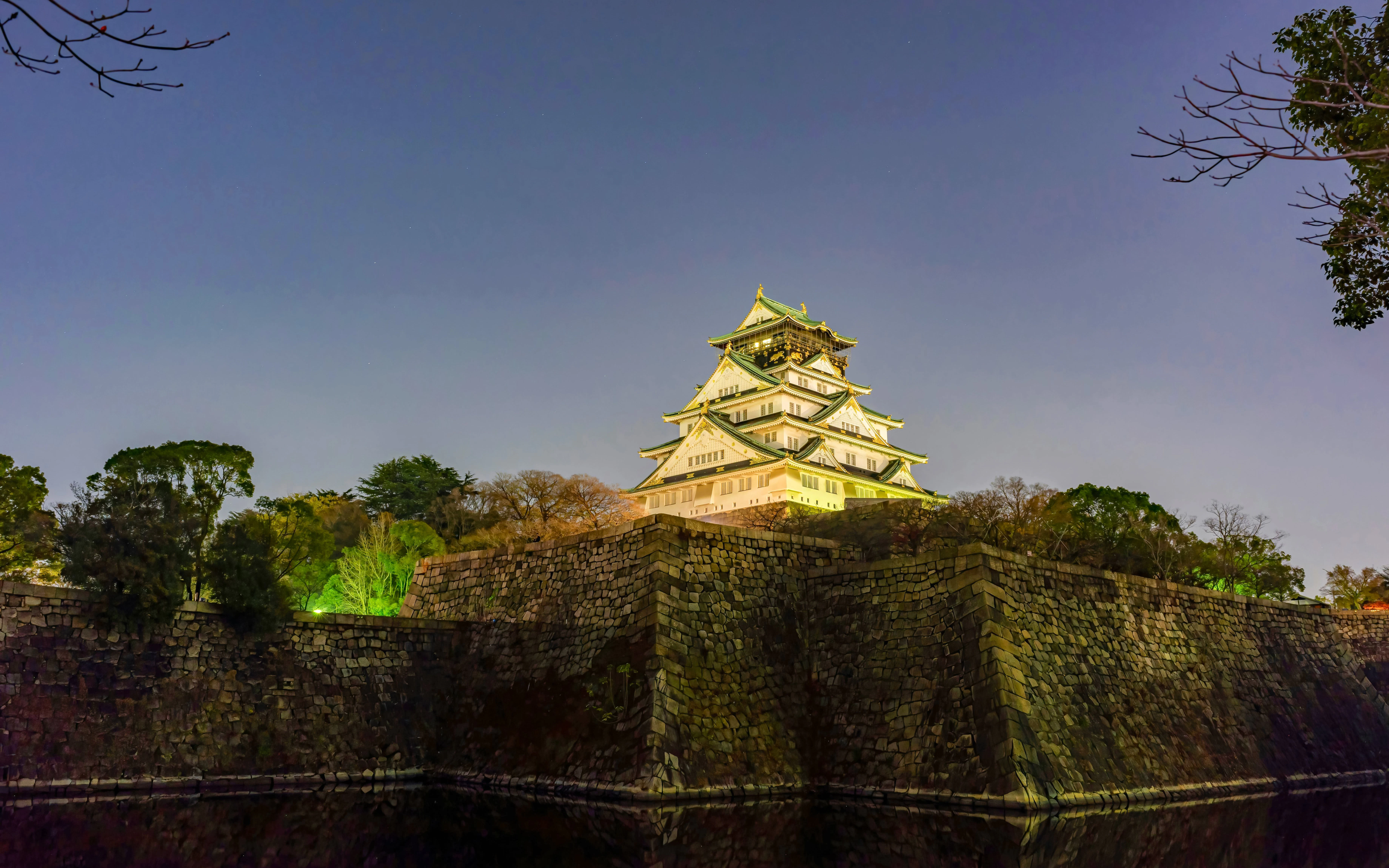 Night view of illuminated Osaka Castle with surrounding stone walls.