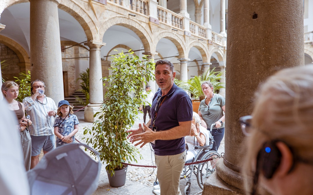Tour guide explaining history at Palazzo Dei Normanni courtyard, Palermo.