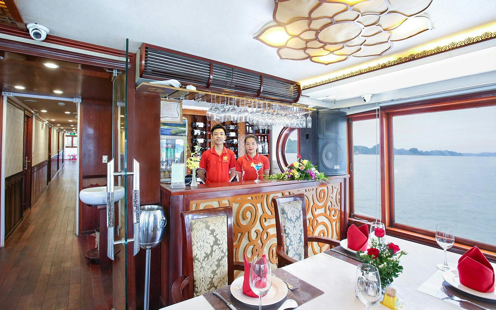 Cruise dining area with staff at bar, Halong Bay view through window.