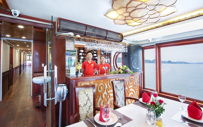 Cruise dining area with staff at bar, Halong Bay view through window.