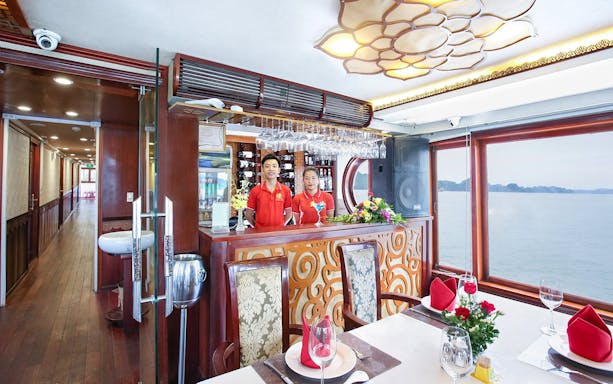 Cruise dining area with staff at bar, Halong Bay view through window.