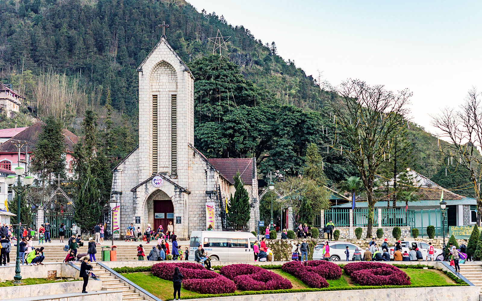 Main square with Notre Dame Cathedral in Sapa, Vietnam, surrounded by visitors and lush greenery.