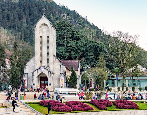 Main square with Notre Dame Cathedral in Sapa, Vietnam, surrounded by visitors and lush greenery.