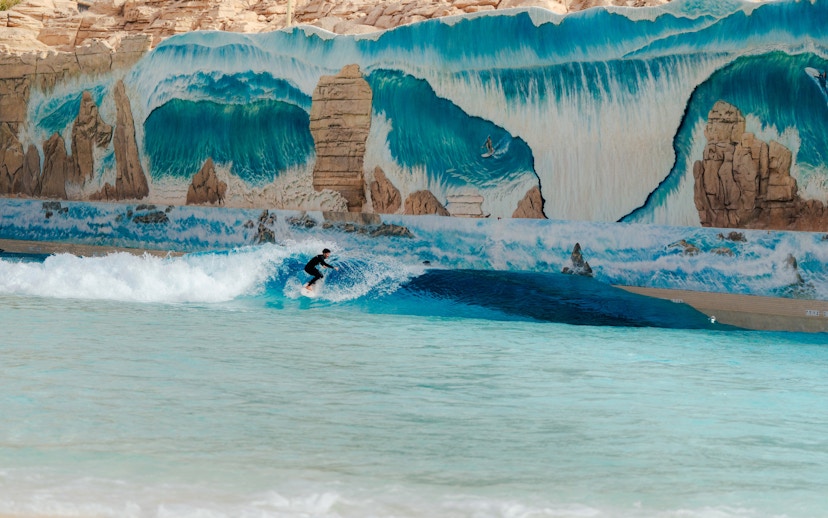 Surfer riding a wave at Surftopia, Saudi Arabia with mural backdrop.