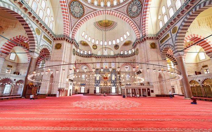 Interior of Suleymaniye Mosque in Istanbul with ornate ceiling and red carpet.