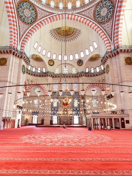 Interior of Suleymaniye Mosque in Istanbul with ornate ceiling and red carpet.