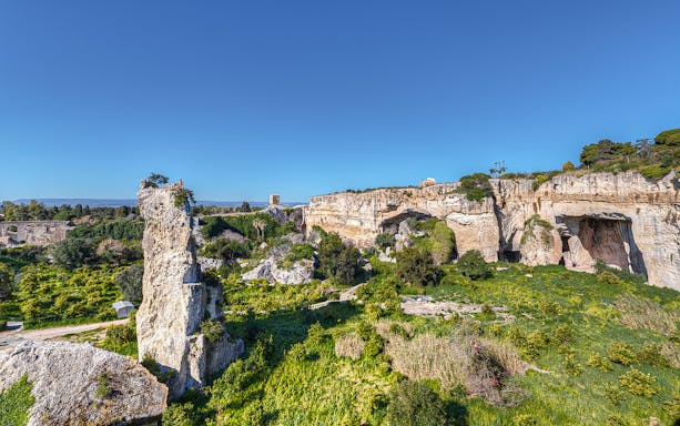Syracuse's Greek Theater and Neapolis archaeological park with rocky landscape and greenery.