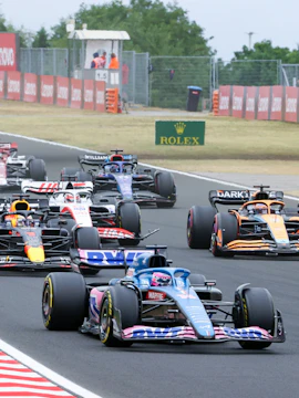Race cars competing at the Hungarian Grand Prix on a track with spectators.