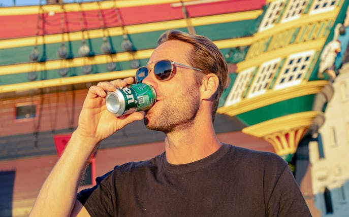 Man enjoying a drink on a party cruise in Amsterdam with a historic ship backdrop.