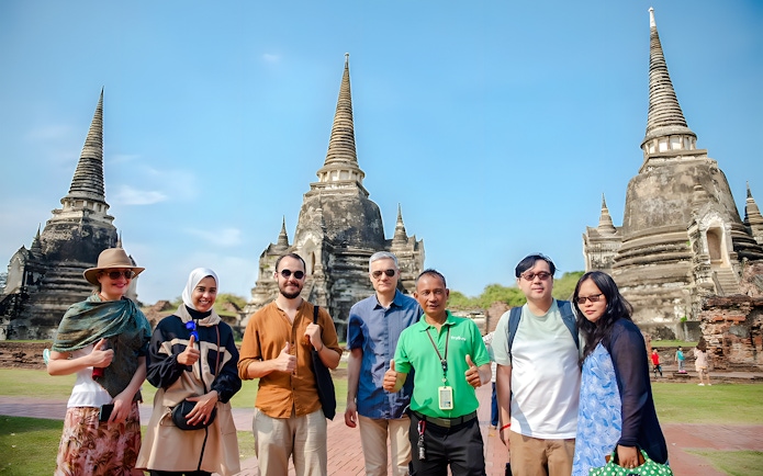 Tourists with guide at Wat Phra Si Sanphet, Ayutthaya, with ancient stupas in the background.