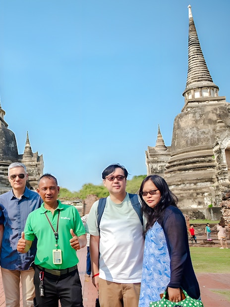 Tourists with guide at Wat Phra Si Sanphet, Ayutthaya, with ancient stupas in the background.