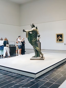 Visitors viewing a statue in a museum gallery.