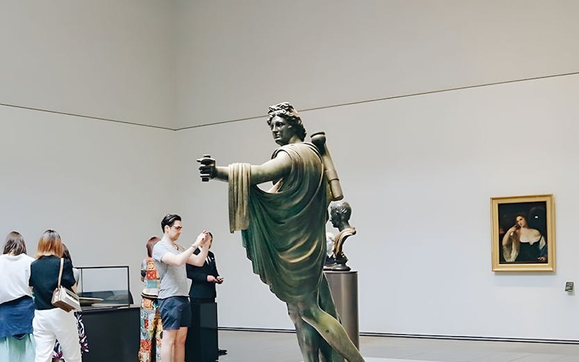 Visitors viewing a statue in a museum gallery.