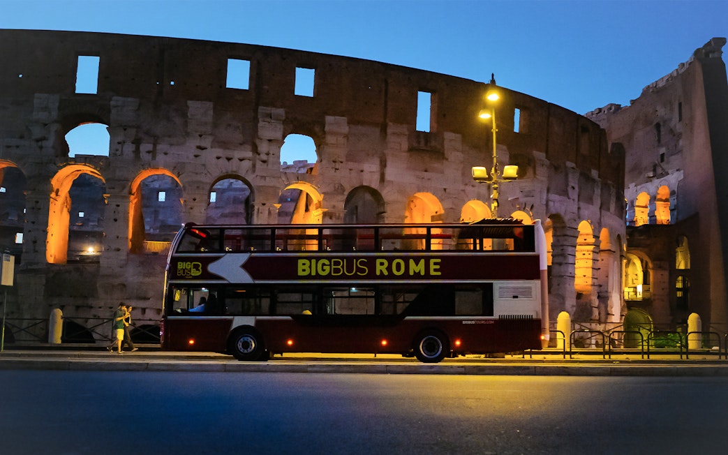 Big Bus tour in front of the Colosseum, Rome, at dusk.