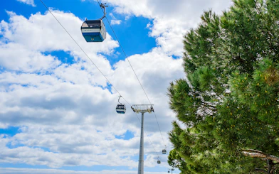 Lisbon cable cars against a blue sky near trees.