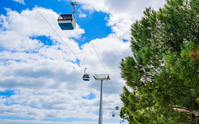 Lisbon cable cars against a blue sky near trees.
