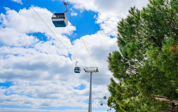 Lisbon cable cars against a blue sky near trees.
